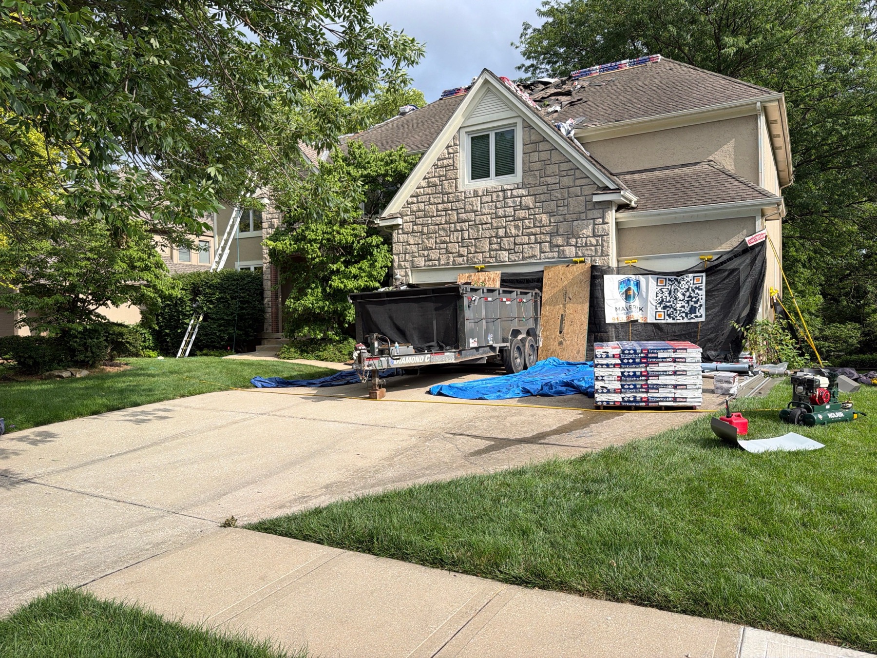 Roofing materials, dump trailer, tarps, plywood, and protection staged on a driveway during roof replacement.