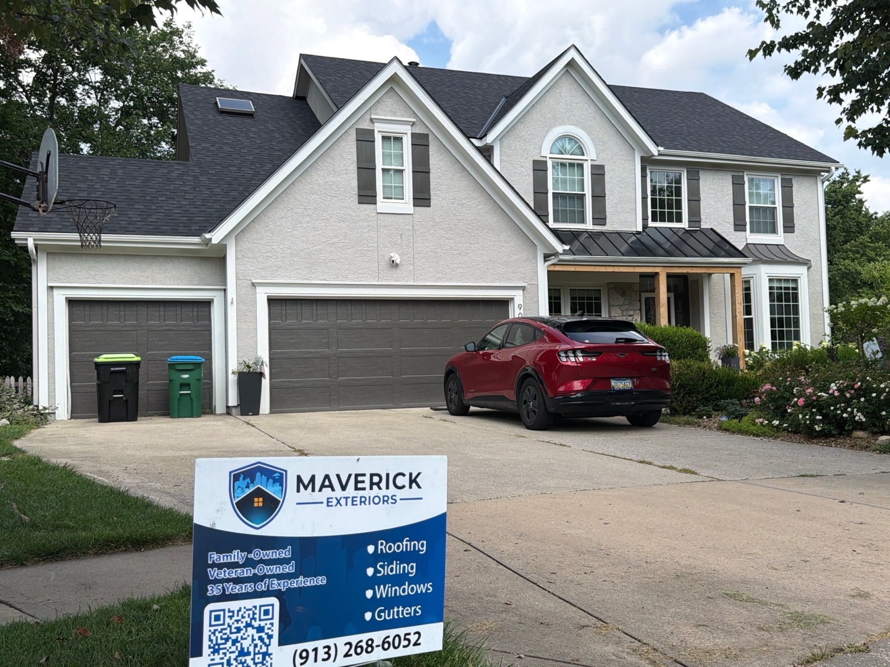 Finished Maverick Exteriors roof replacement with yard sign in front of a large Kansas City metro home.